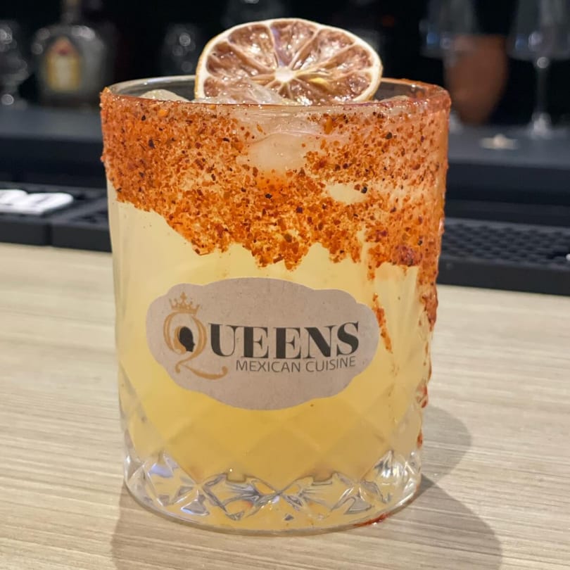 A Queens Mexican Cuisine cocktail with a chili-lime rim and a dried citrus slice.