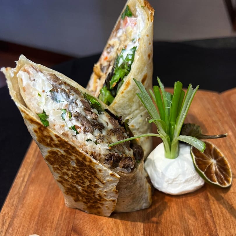 Two large burritos filled with meat, rice, and white sauce, garnished with green onions and lime.