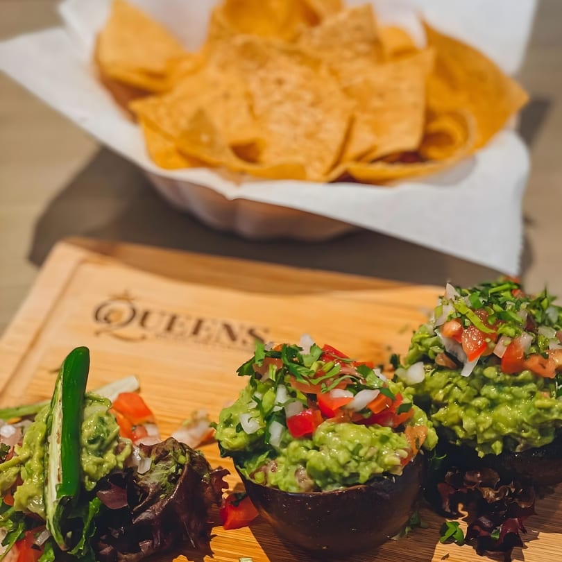 Fresh guacamole in avocado halves with pico de gallo and tortilla chips at Queens Bar & Grill.