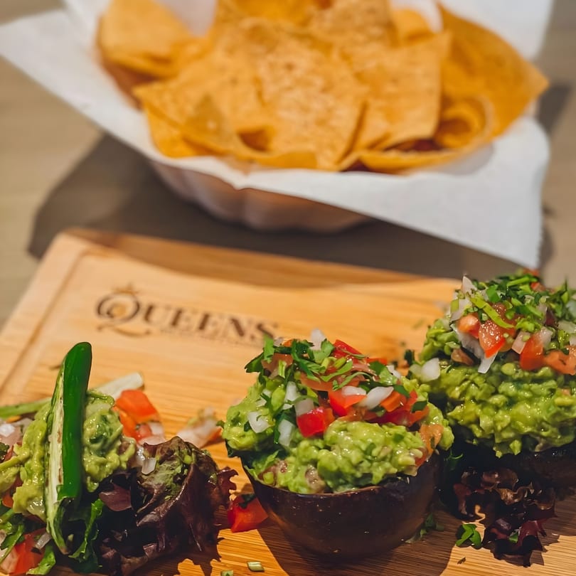 Fresh guacamole with pico de gallo and tortilla chips on a wooden board at Queens Bar & Grill.