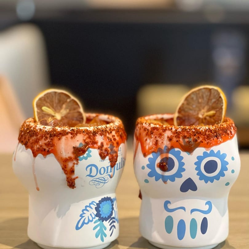 Two skull-shaped cocktails with red chili rim and dried orange slices at Queens Bar & Grill.